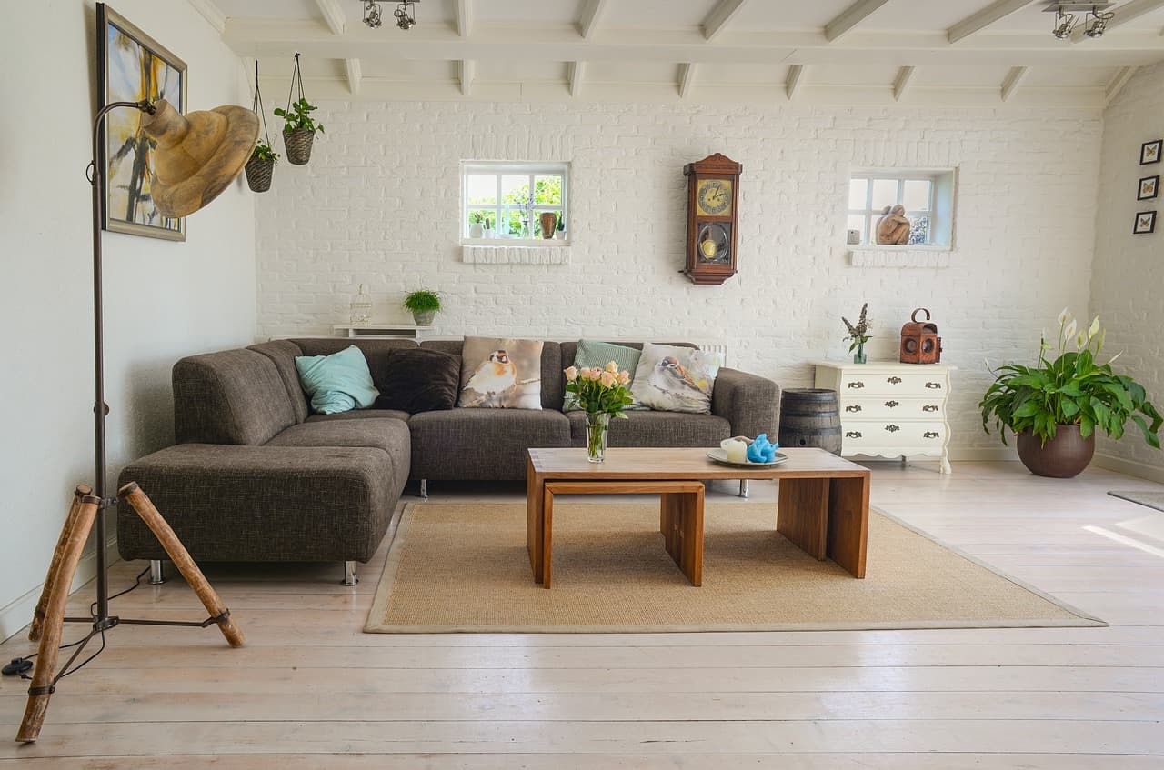 A bright living room with a corner sofa, white-painted brick and timber beams