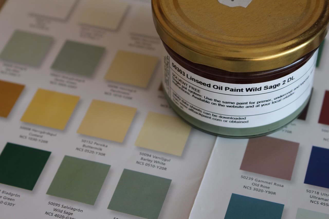 Paint colour cards in greens, yellows and pinks beside a tin of sage paint
