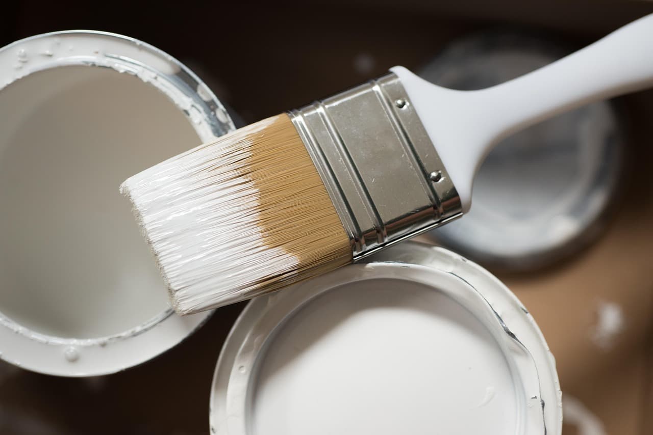 A brush loaded with white paint over an open tin